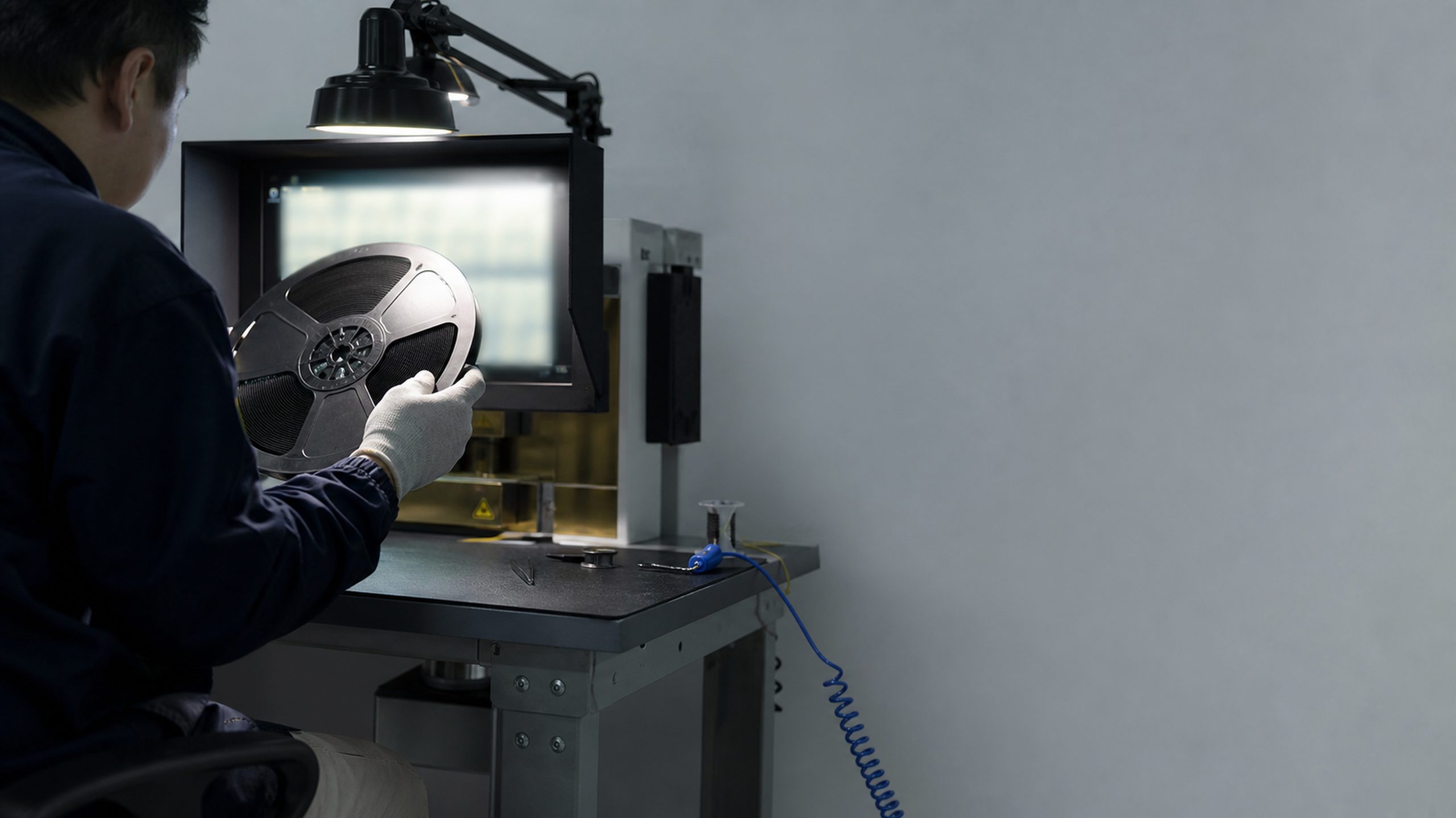A technician at an ESD bench holding a tape-and-reel of components up against a reference screen.